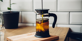 A French press on a wooden cutting board in the process of making cold brew coffee, with coffee grounds steeping in cold water, exemplifying the method of refrigerating for 12-15 hours to achieve a smooth and delicious cold brew at home.